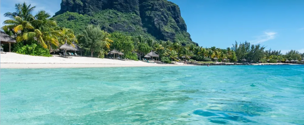 The beach at Le Morne with palm trees, a turquoise lagoon and the Le Morne Brabant mountain behind it